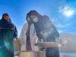 With the backdrop of a mountain, one among three Afghan women lifts the lid of a cooking pot